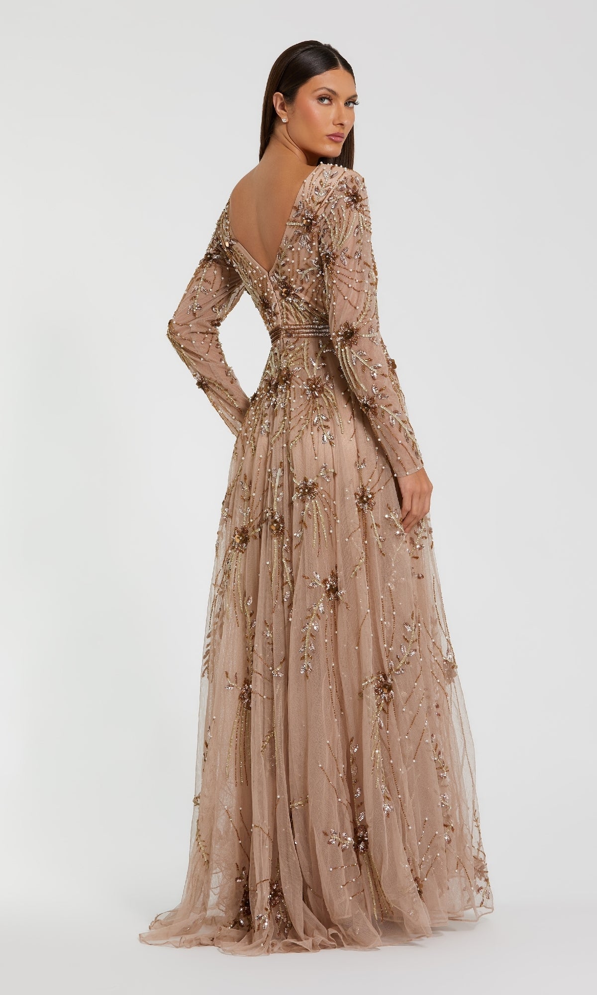 A woman models the Mac Duggal 6086 Long Sleeve Beaded Formal Gown, featuring intricate beadwork and floral embellishments, standing with her back slightly turned against a plain white background, radiating elegance.
